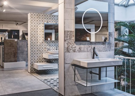 Designorientiertes Badstudio mit großem rechteckigem Waschtisch, rundem LED-Spiegel und grafisch gemusterten Wand- und Bodenfliesen.